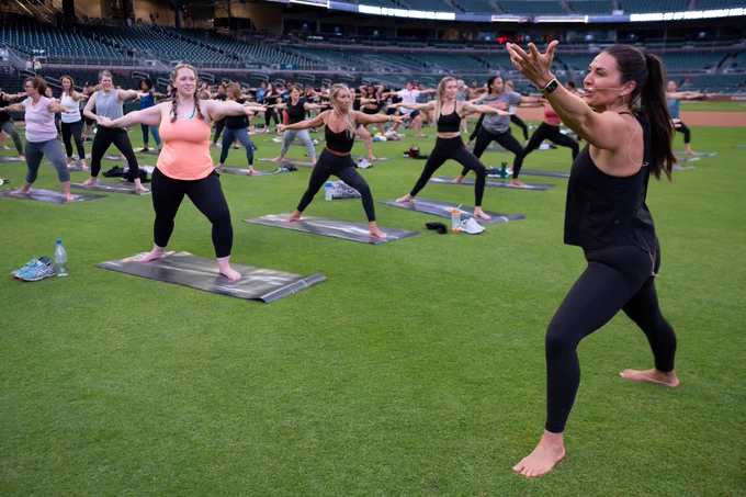 Yoga instructor demonstrates a pose for attendees during yoga class on field at Truist Park