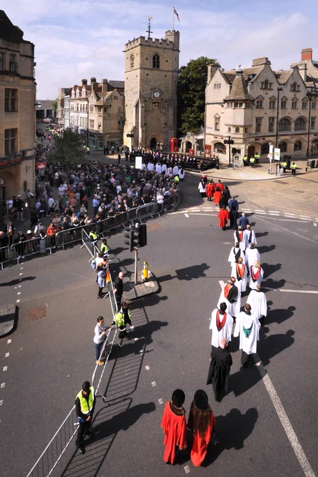 Image of robed officials from Oxford City Council walking towards Cafax Tower as crowds gather for the proclamation service of King Charles III. 