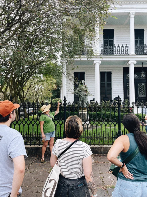 Tour guide pointing to historic white Italianate house in the Garden District with people standing in front.