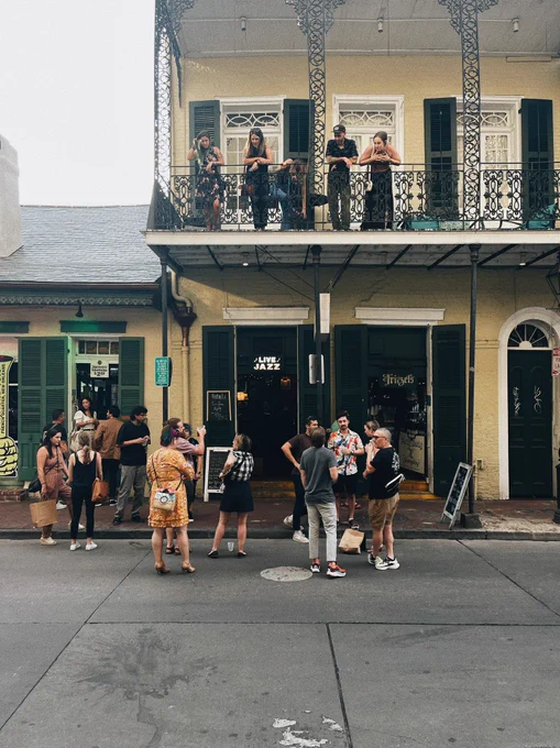 A group of people standing on Bourbon Street with some up in the gallery and some in the street.