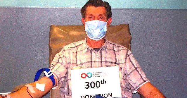 a man wearing a mask donating blood while holding up a 300th donation sign