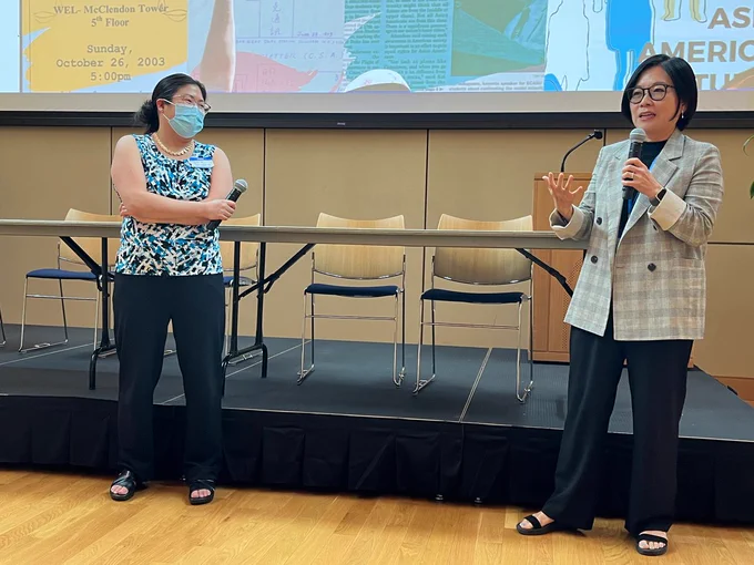 Heidi Kim of UNC holds a microphone, smiling at Esther Lee, who gestures while speaking into her microphone to attendees