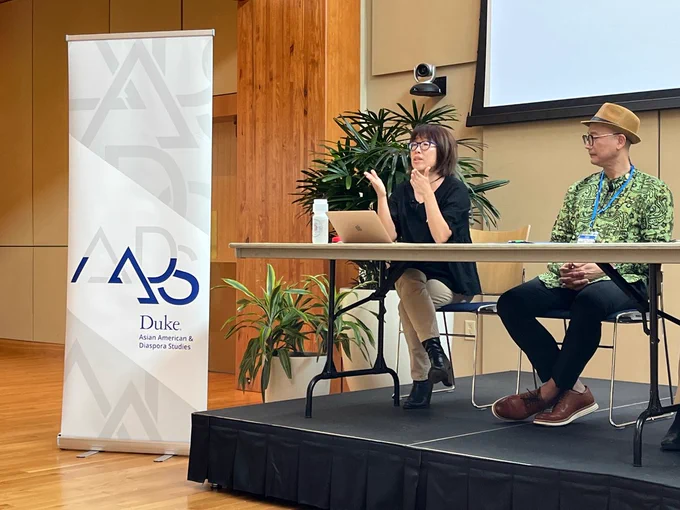 Aimee Kwon extends both her hands toward the audience while speaking from her seat on stage during a panel discussion. Francis Tanglao-Aguas sits to the right, facing toward her with his hands in his lap.