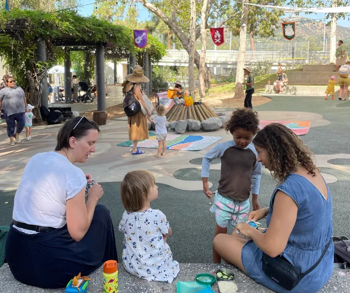 Adults and children having a snack around a play campfire