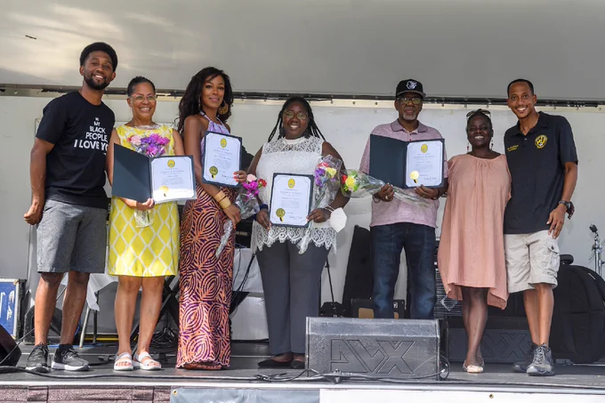 Baltimore City Mayor Brandon Scott stands onstage with six other people, all smiling for the camera. Four of them are holding certificates.