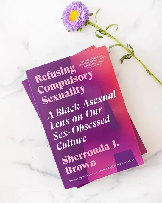the book, Refusing Compulsory Sexuality: A Black Asexual Lens on Our Sex-Obsessed Culture, next to a purple flower. 
