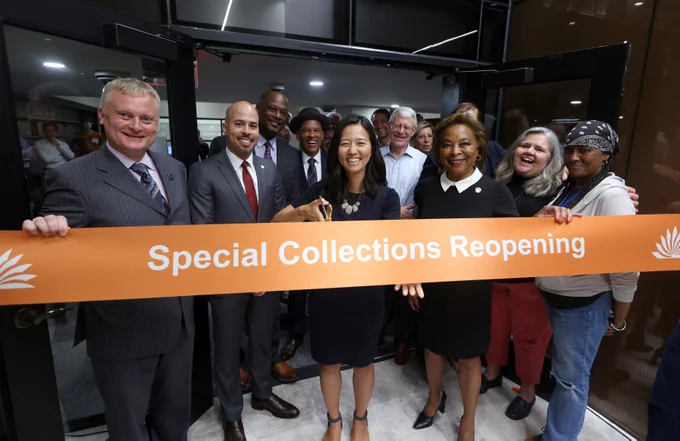 Mayor Wu is surrounded by BPL leadership and community members to cut an orange ribbon that says "Special Collections Reopening". 