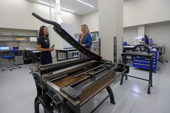 Mayor Wu and a BPL staff member stand behind a large mechanical library tool with a lever attached. 