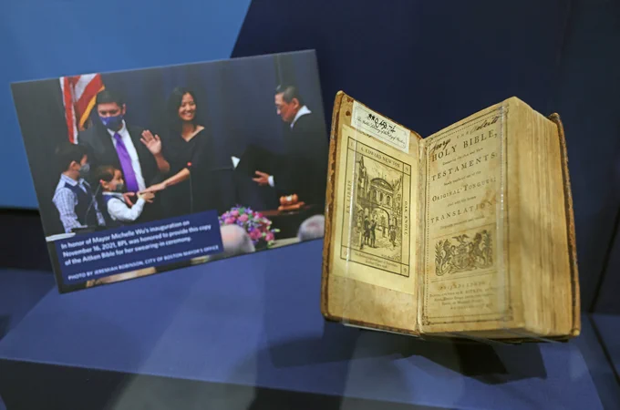 An aged bible open to the first page rests next to a photo of Mayor Wu's swearing-in ceremony, both behind a glass case.