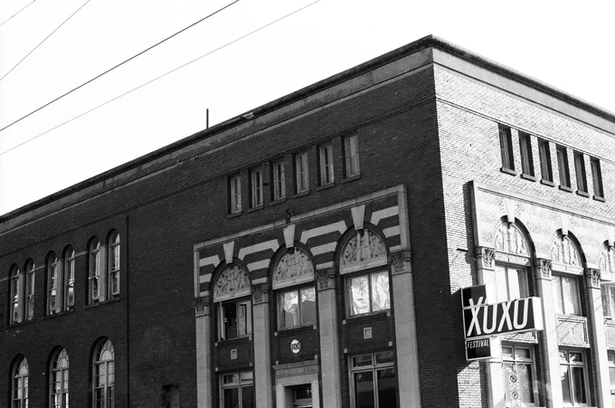 Black-and-white photo of the Yale Union Laundry Building, a two-story brick industrial building in Portland, Oregon. A large marquee saying "XOXO Festival" hangs off the side.