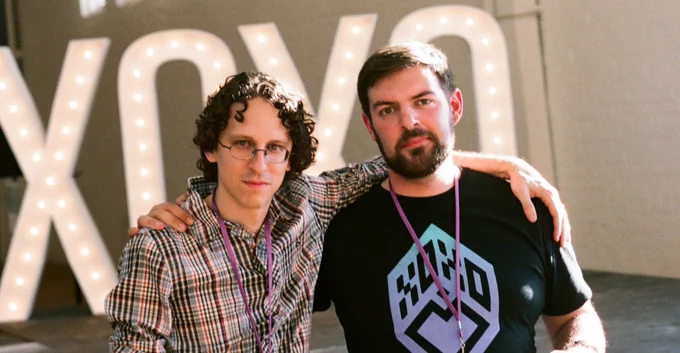 Photo of exhausted XOXO founders Andy Baio and Andy McMillan sitting side-by-side in front of illuminated "XOXO" letters on stage at the end of the first XOXO.