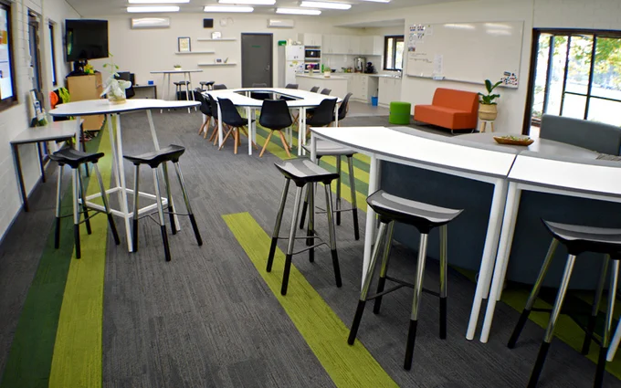 3 views of Vasse Primary School's staffroom, showing tables that form a large oval, a semi-circular group of lounges with a table in the middle and perch tables and stools around the back of the lounges. There are also pot plants, storage shelves and a small kitchen in the distance.