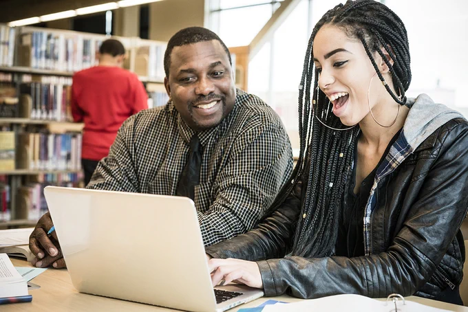 A teacher and student looking at a laptop together in a library.