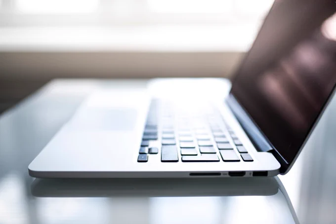 side view of a silver laptop with black keys, fading out of focus with a brightly lit window in the background