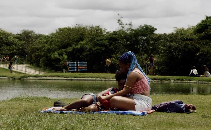 An AfroBrazilian woman with blue hair holds another AfroBrazilian woman while seated on a blanket in a park. From Mars One