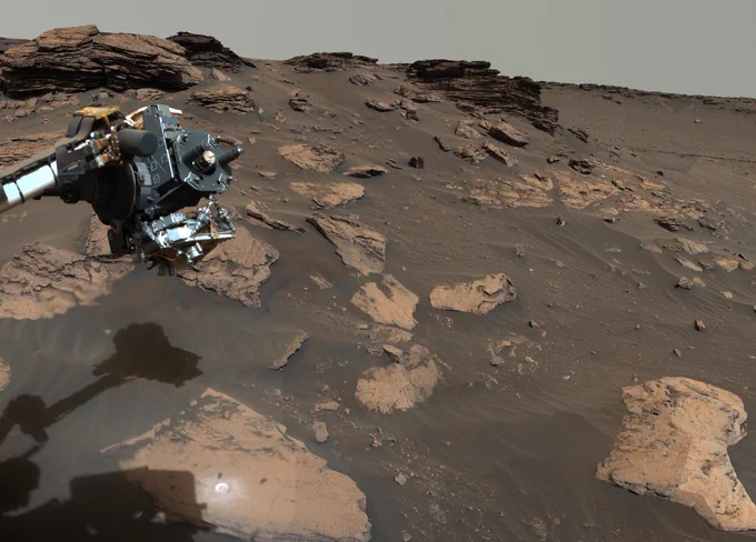 Photo from NASA's Perseverance rover shows a rocky slope, with two drill holes visible in a flat, foreground rock. Part of the rover's robotic arm -- and its shadow -- are visible at the left.