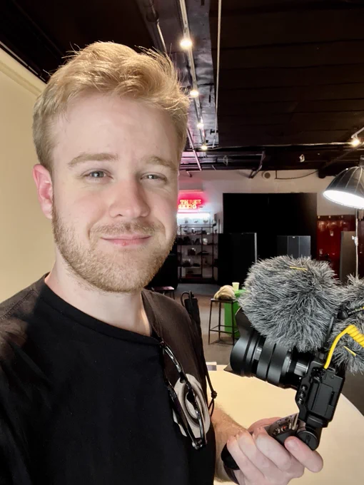 In a production room James slightly smiles for a selfie holding his vlogging camera, a Sony ZV-e10 with a Duo4 Microphone.