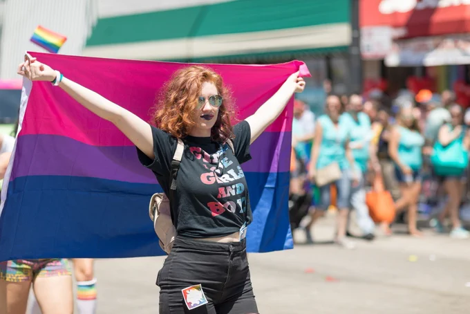 Photo from istock.com/Roberto Galan featuring a person at a Pride event raising the bisexuality flag behind them.