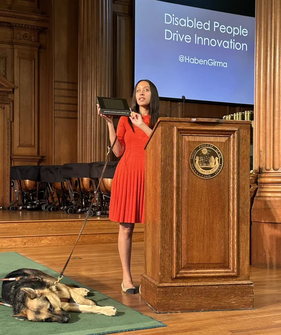 I’m standing in a gorgeous, ornate wood chapel beside a lectern that says Phillips Academy. I’m holding up my braille computer to show it to students, and Seeing Eye dog Mylo is stretched out on the floor by my feet. A monitor behind me says, “Disabled People Drive Innovation.”