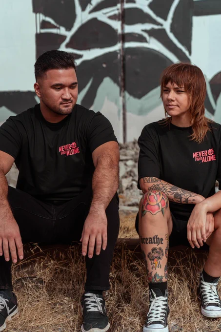 Two people sitting down, they are wearing the Never Fight Alone black tee with the red logo.