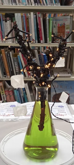 Crystals hanging on twig decorated with lights and sitting in a conical flask.