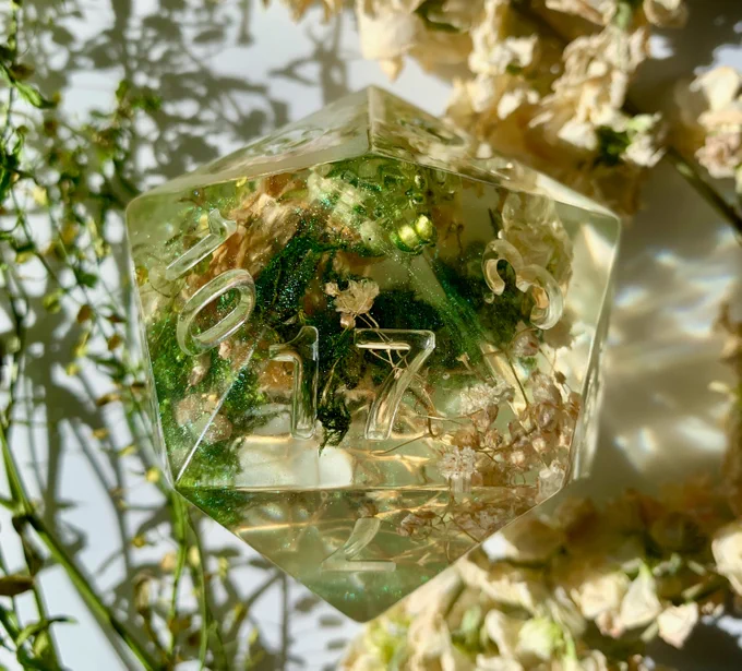 Twenty sided dice used for TTRPG games like Dungeons and Dragons. This dice contains moss, flowers, and swirls of green mica powder.