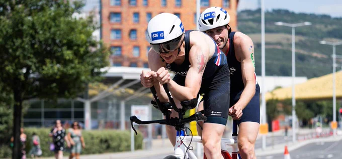 Two male para-triathletes competing in a triathlon race. Riding a tandem bicycle during the cycle.