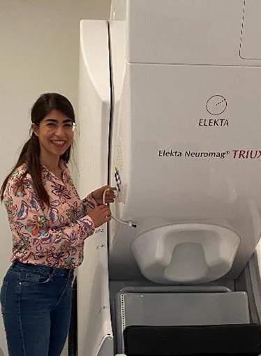 Tara Ghafari stands next to the CHBH's MEG. Tara is a postdoctoral researcher working at the CHBH implementing the MEG studies associated with the mTBI PREDICT consortium.