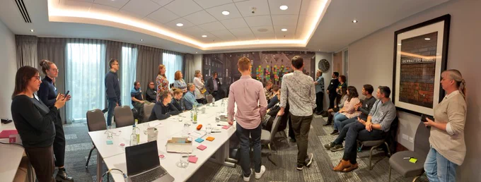 Group of people standing and sitting around a long table in a meeting room 
