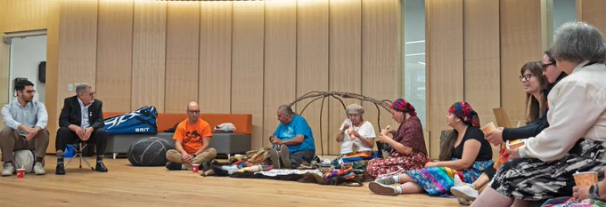 10 people sit as part of a circle as Elders conclude a pipe ceremony.