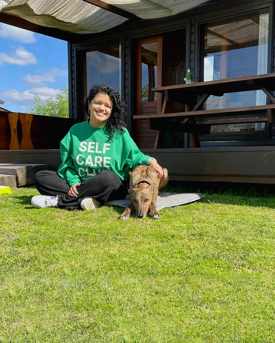 Paula sitting on the grass outside wearing a green sweatshirt with her dog next to her.