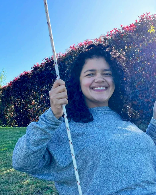 Paula in a blue shirt swinging on a swing outside with a blue sky behind her.
