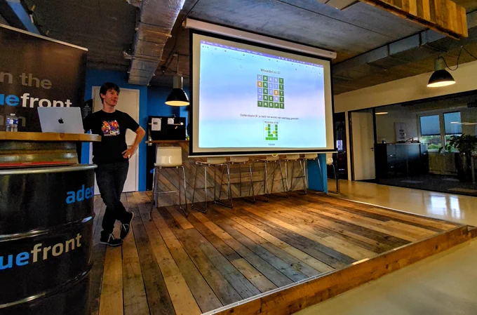 Oliver (the speaker) standing casually in front of a projected slide showing a completed Dutch wordl puzzle