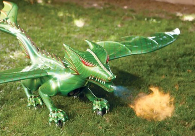 A small dragon toy, probably 2 feet from head to tail, sitting on the grass and soaring in the air, breathing fire.