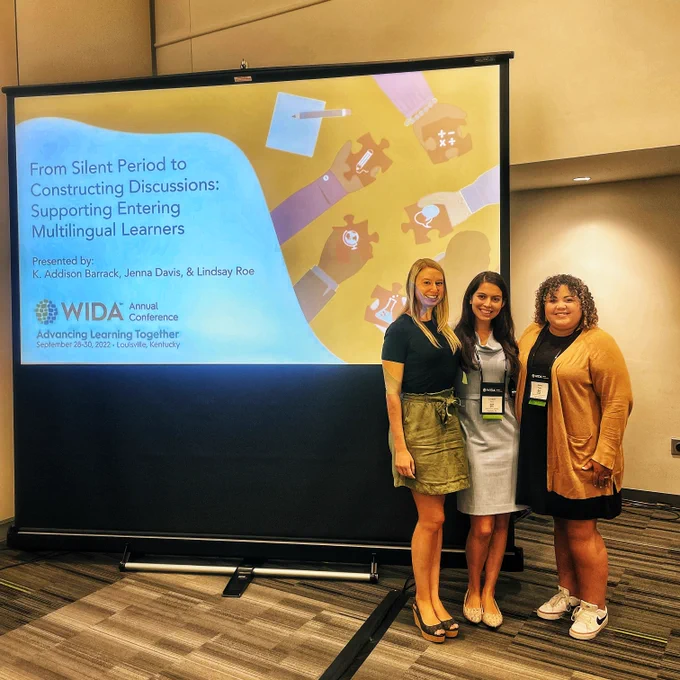 A portrait of co-presenters Addison Barrack, Lindsay Roe, and Jenna Davis all standing before a large screen that displays the abridged text, "From Silent Period to Constructing Discussions: Supporting Entering Multilingual Learners, WIDA, Annual Conference, Advancing Learning Together."