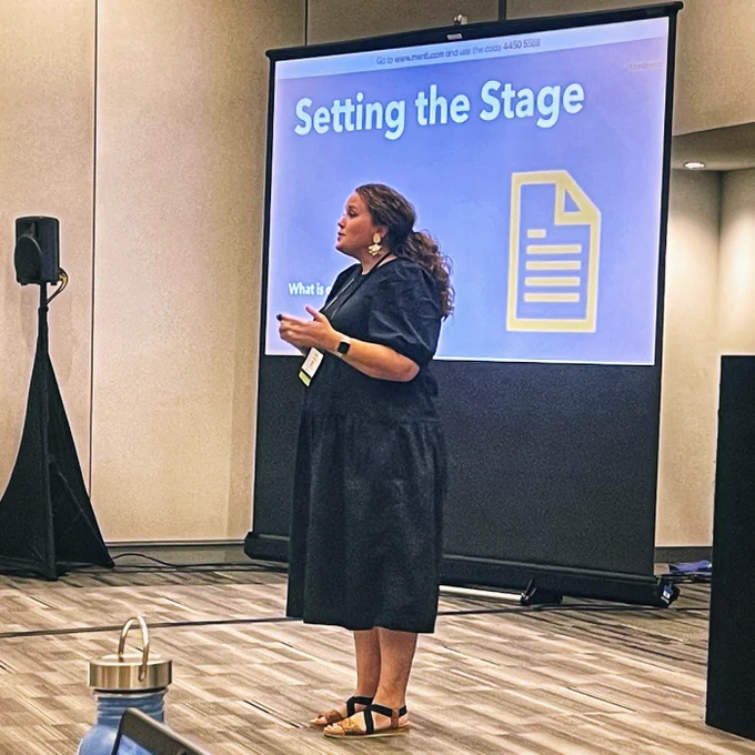 A portrait of presenter Lauren Binkley standing before a large screen that displays an icon of a piece of paper and the abridged text, "Setting the Stage."