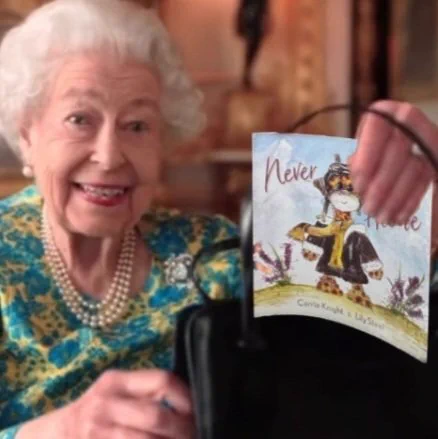 Queen Elizabeth is smiling and holding a copy of the charity book, Never Alone, which she has taken out of her handbag.