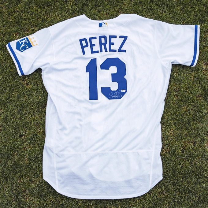A photo of a Salvador Perez signed white Royals jersey laying in the grass at Kauffman Stadium.