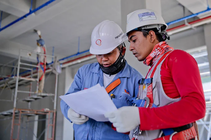 Two skilled trades workers with hard hats reviewing documents together in the workplace.