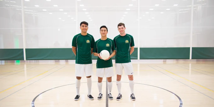 A group of 3 students pose for a photo holding a soccer ball. 