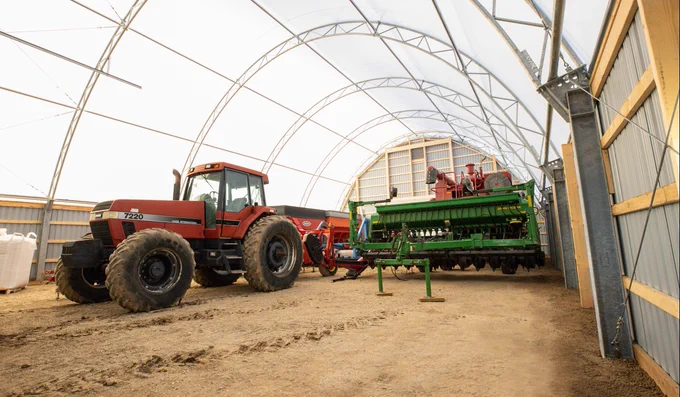 Interior view of a fabric building with a steel-framed structure that has tractors and farming equipment stored inside. 