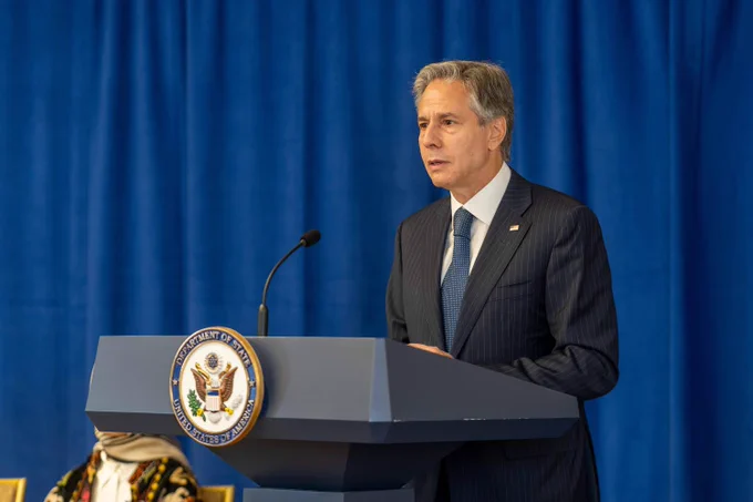 Secretary of State Antony Blinken stands on a podium with the U.S. Department of State emblem on the middle. He is speaking into the microphone announcing the State Departments Alliance for Afghan Women’s Economic Resilience.