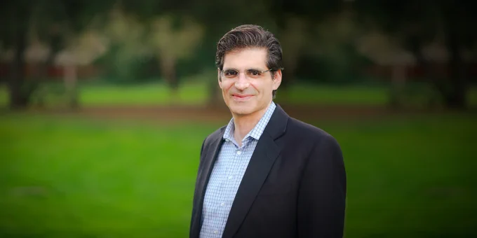 Headshot of Josh Becker wearing glasses, a black jacket and blue pin striped shirt