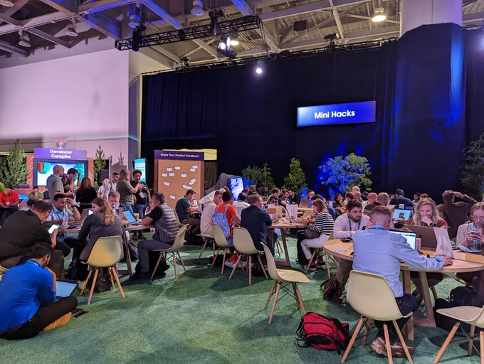 Developers sitting at tables at an event doing coding activities 