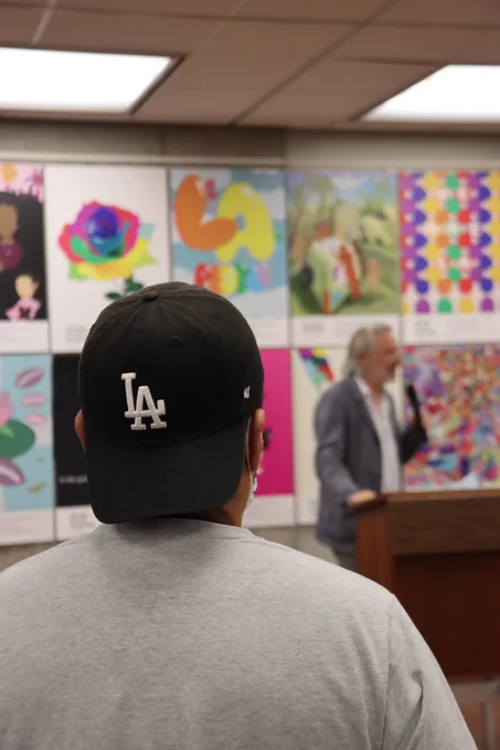 Student with LA cap in foreground and Dean Trzaskoma in the background among student artworks.