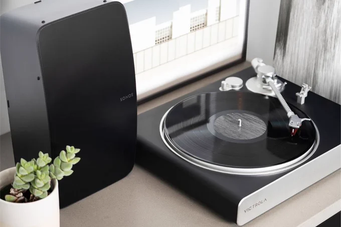 A Sonos Five speaker sits next to Victrola's new Stream Carbon turntable next to a framed photo and a potted succulent.