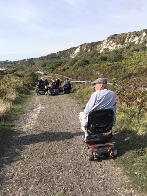 Norman in his wheelchair sits behind the rest of the group on a track coming up to a view of the sea.