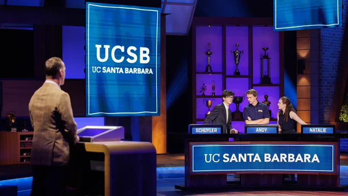 Three UC Santa Barbara students (Schuyler, Andy, and Natalie) stand behind their podiums on the set of the College Bowl show discussing the answer to a question before sharing it with host Peyton Manning.
