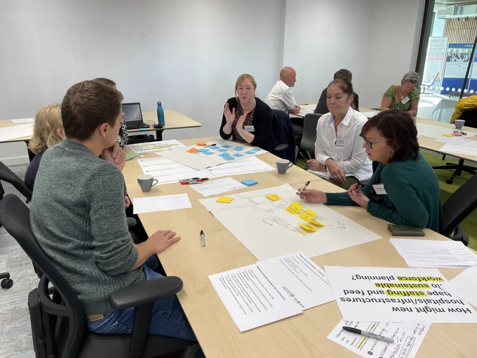 A group sit around a table writing on post-it notes and paper