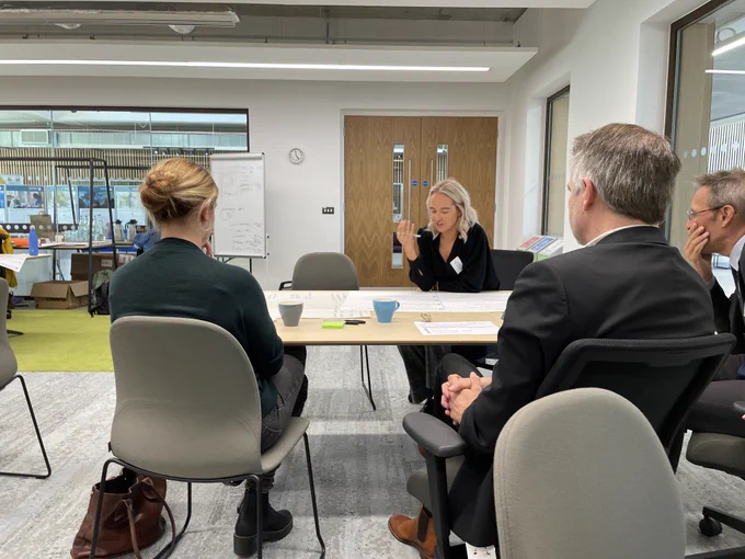 A group of people around a table share their ideas with the room